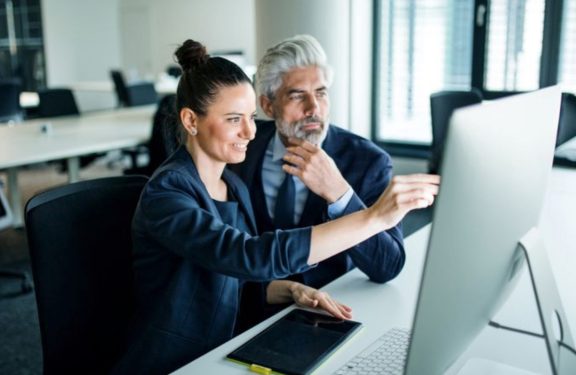 Woman pointing out something on computer screen while older man in suit listens