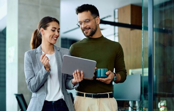Professional woman sharing tablet screen with man wearing glasses and holding a coffee cup