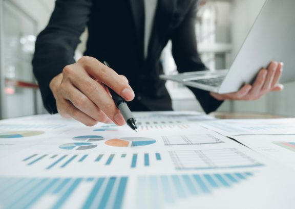Man holding laptop in one hand and marking notes on a graph with a pen
