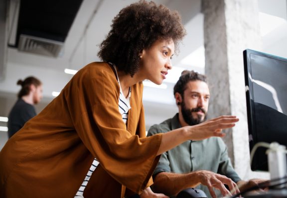 Professional woman reviewing screen and providing feedback to man at computer